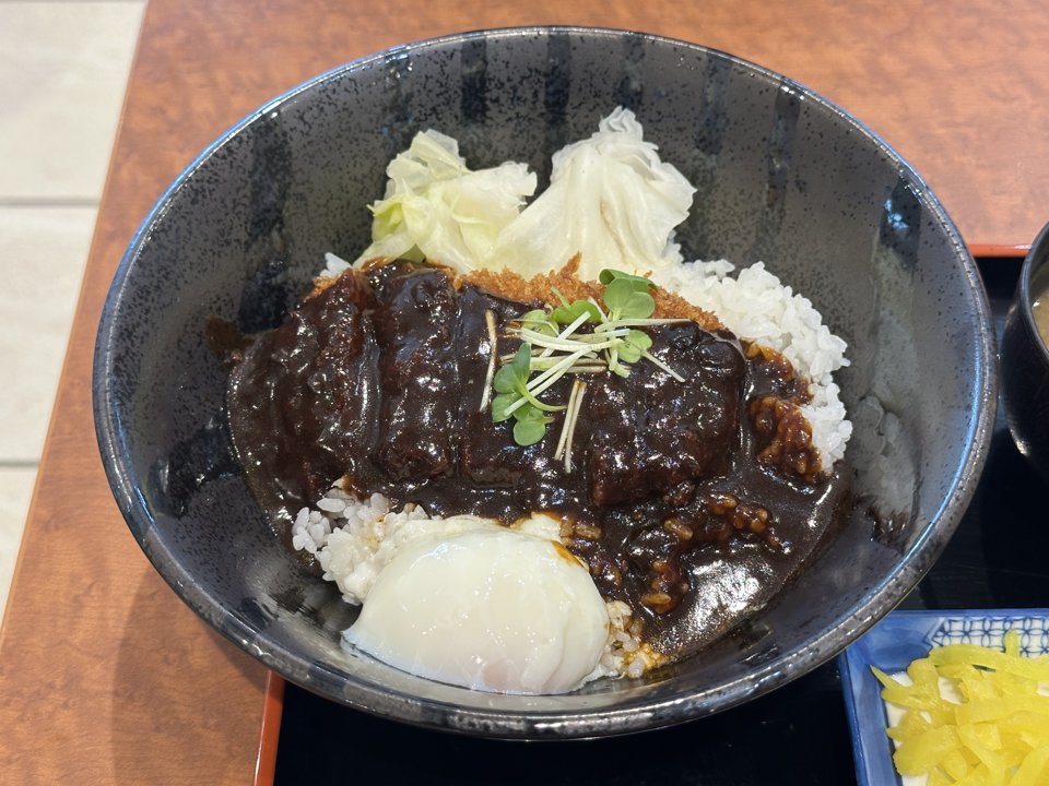黒い丼にご飯、キャベツ、デミグラスソースをかけたカツと温泉玉子。吉備サービスエリア下り線で2026年9月撮影。
