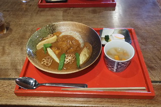 赤いトレーに置かれた、野菜を添えたカレーとご飯、スープと小皿