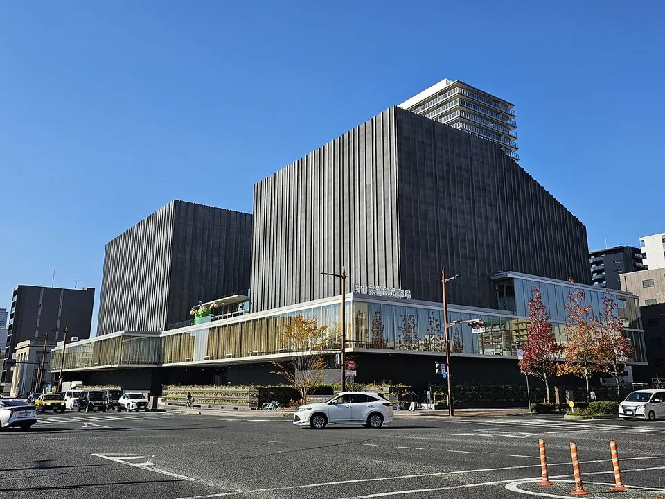 青空の下、縦のラインを持つ壁とガラス張りの低層部分がある岡山芸術創造劇場ハレノワの外観