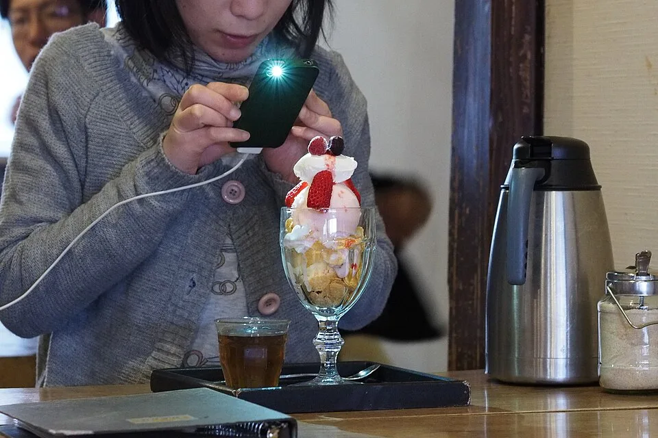 三宅商店のテーブルに置かれたいちごの載ったパフェと飲み物、スマートフォンで写真を撮る人