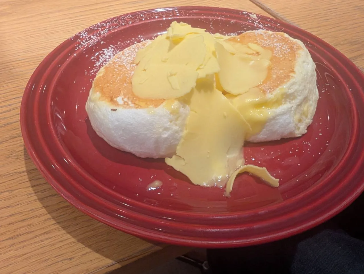 赤い皿に載ったふわっとしたパンケーキ。上に薄いバターがたっぷりのっている。