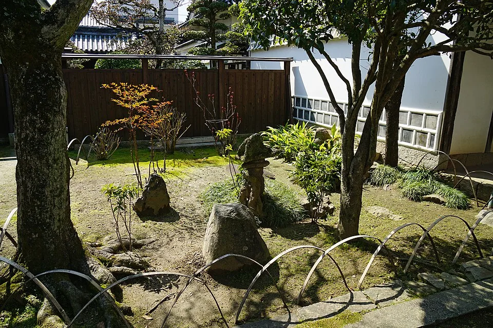 白壁の建物の前に石と樹木が並ぶ旧矢掛脇本陣の庭